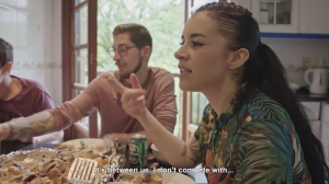 group of people eating a meal inside a kitchen in conversation