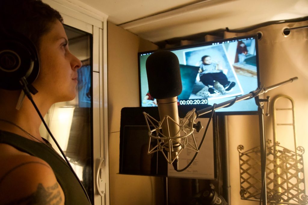 woman in recording studio in front of microphone watching video on monitor