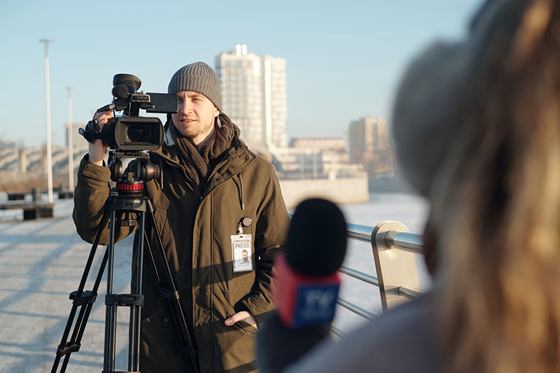 Male operator shooting news reportage Focus on young male operator or videographer shooting female reporter with microphone while shooting news reportage